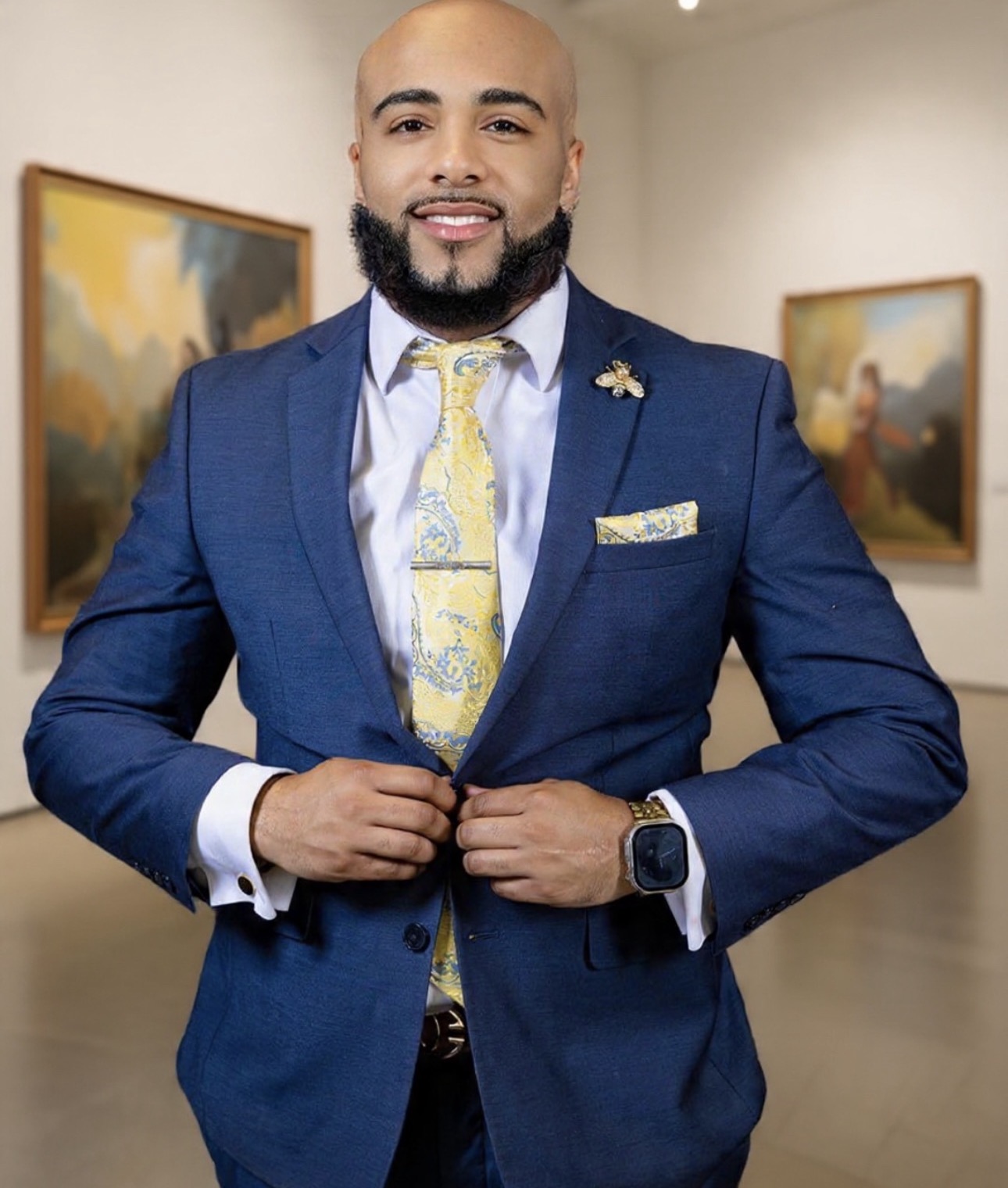 Brandon Anthony in a navy suit with a yellow patterned tie, adjusting his jacket